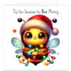 Bee-themed Christmas card featuring a cute yellow and black bumblebee with large sparkling eyes, rosy cheeks and blue wings, wearing a red Santa hat and wrapped in colourful glowing Christmas lights. Dark green text above reads "'Tis the Season to Bee Merry" on a clean white background.