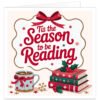 Book lover Christmas card on a soft cream background featuring the festive message “’Tis the Season to be Reading” in flowing red lettering. A large red bow and wavy gold border frame the text, with gold snowflakes and stars around the design. At the bottom, a steaming festive mug sits beside a stack of red and green books decorated with snowflakes, stars, holly and red berries. Cosy Christmas card for readers and bookworms.