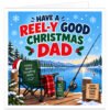 Funny fishing Christmas card for Dad featuring the text “Have a Reel-y Good Christmas Dad”. Colourful winter lakeside scene with snowy pine trees, mountains, fishing rod and float. A green fishing chair with tartan blanket and Santa hat sits on a wooden jetty beside a flask reading “Eat Fish Relax Repeat”. Includes holly, snowflakes and a “Good Fishing Good Times” sign.