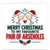 Funny rude Christmas card for a couple featuring the text “Merry Christmas to My Favourite Pair of A***holes”. Modern white design with two clinking wine glasses wearing red Santa hats, a small red heart and festive holly with berries. Red, green and black typography creates a bold adult humour design, ideal for a married couple, husband and wife, partners, boyfriend and girlfriend.